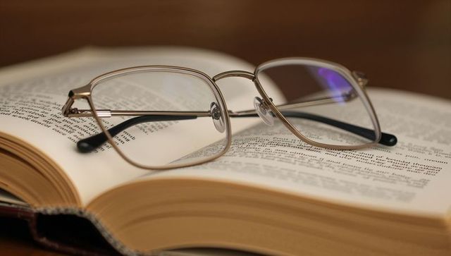 Metal-Rimmed Reading Glasses Resting on Open Paperback Book with Soft Purple Reflection