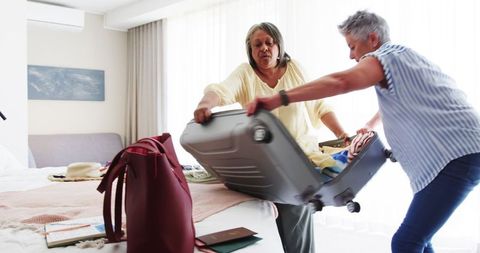 Senior lesbian couple packing suitcase in hotel room for vacation