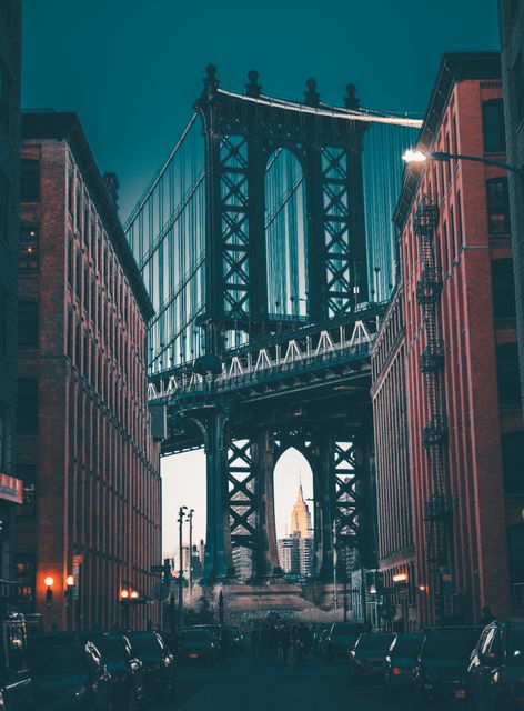View of Manhattan Bridge from Dumbo neighborhood in Brooklyn, New York City, with Empire State Building centered under the bridge arch at dusk. Ideal for content related to travel, architecture, iconic city landmarks, and urban life.