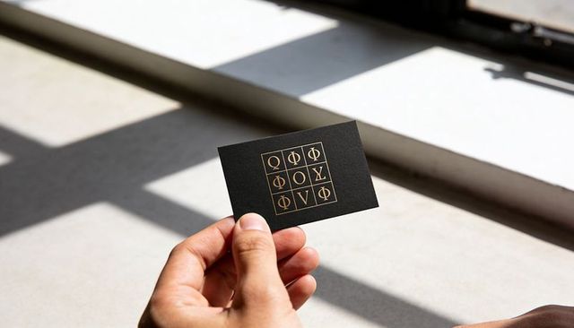 Holding black business card with gold geometric grid and ancient glyphs