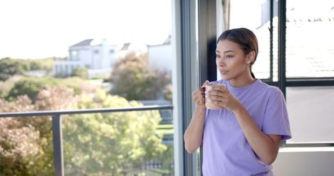 Morning Refreshment: Woman Enjoying Coffee on Balcony in Purple Shirt