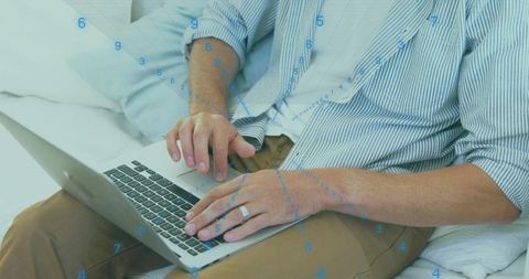 Mature Man Typing on Laptop from Bed Wearing Striped Shirt and Khaki Pants