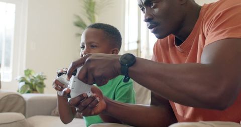 Father and Son Playing Video Games on Couch Bonding Over Controller in Bright Living Room