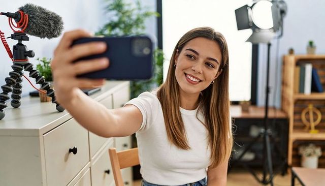 Female creator filming selfie in home studio with smartphone, microphone, softbox lighting