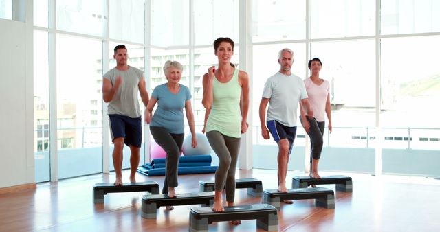 A diverse group of adults, including seniors, is engaging in a step aerobics class at a gym. They appear focused and energized, using steps to follow the exercise routine. This can be used in materials promoting fitness classes, active lifestyles, senior health programs, and community wellness initiatives.