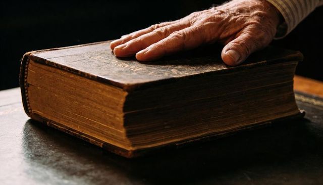Elderly Hand Resting on Antique Leatherbound Book with Gilded Pages