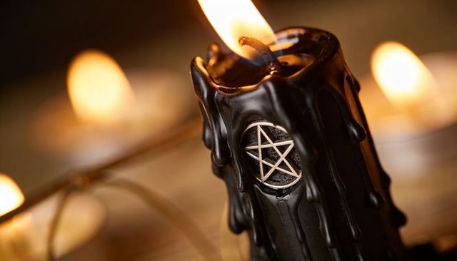 Closeup black ritual candle melting wax with pentagram medallion and warm bokeh candlelight