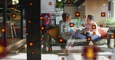 Women collaborating and sharing tablet in modern coworking lounge with social media icons