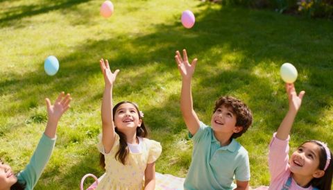 Children tossing pastel eggs on sunny lawn during spring picnic
