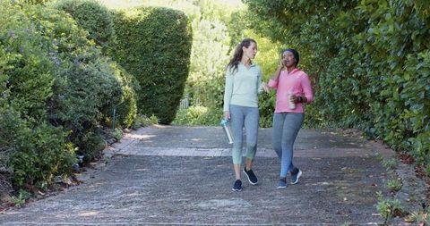 Diverse female friends strolling garden path discussing happiness