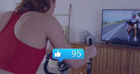 Woman cycling on stationary bike streaming spin workout with social likes overlay at home