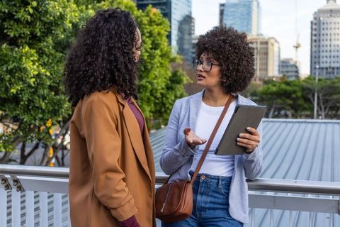African american women discussing business strategy on urban terrace holding tablet