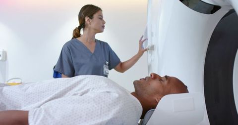 African american patient undergoing ct scan with female technologist operating scanner