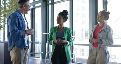 Diverse Coworkers Collaborating in Bright Office, Woman in Green Blazer Holding Phone