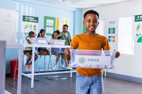 African american boy holding paper recycling bin during classroom recycling lesson