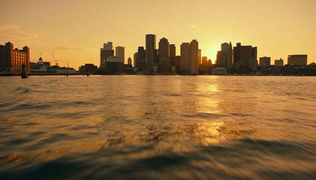 Golden skyline silhouette over harbor at sunset reflecting amber light on rippled water