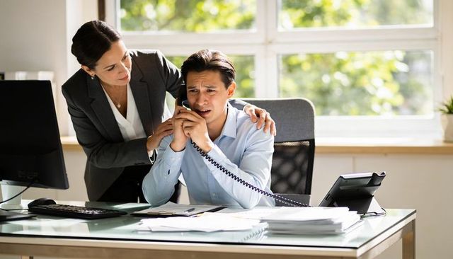 Worried office worker receiving colleague support during stressful phone call at desk