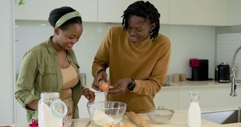 African american couple baking together on kitchen island mixing batter and cracking eggs