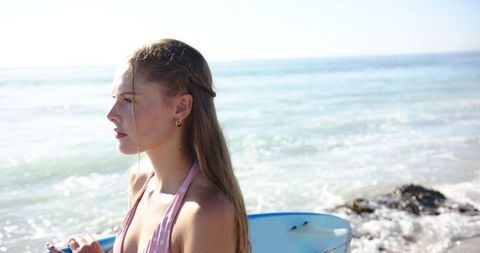 Young Woman Gazes at Sea with Surfboard in Contemplation of Surf Adventure