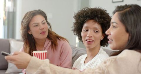 Multicultural friends sharing popcorn and laughing on cozy living room couch
