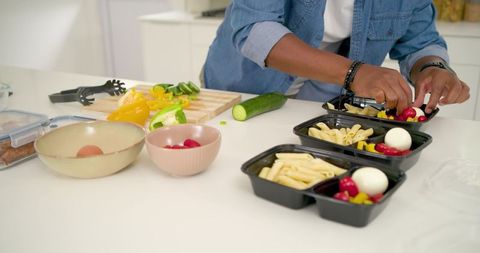 African american man preparing healthy meal prep containers with penne, eggs, veggies