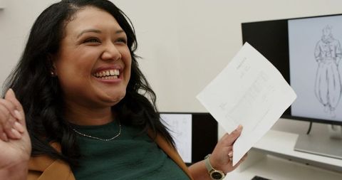 Joyful professional woman celebrating design approval, smiling and holding document at desk