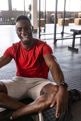 African american man laughing and checking smartwatch while sitting on gym floor