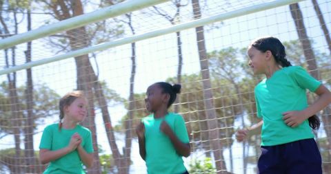 Youth girls celebrating at soccer goal wearing teal shirts on sunny outdoor field