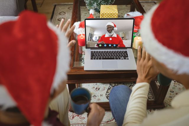 Diverse couple with santa hats having video call with happy african american man with santa costume. Christmas, celebration and digital composite image.