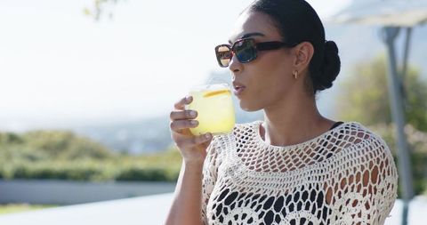 African american woman sipping lemonade on sunny terrace in crochet top and sunglasses