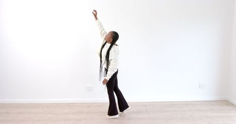 Woman with Long Braids Reaching Upward in Minimalist Room