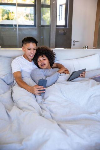 Diverse Couple Relaxing with Technology in Modern Bedroom