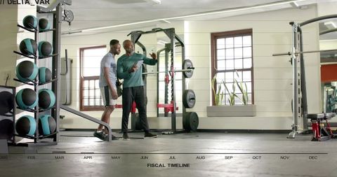 Trainer guiding client at squat rack in modern gym, weightlifting coaching session