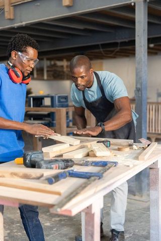 African american coworkers cutting wooden planks at workshop workbench with cordless drill