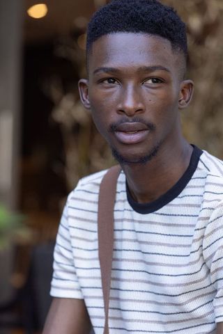 Contemplative african man gazing left in cafe wearing striped t-shirt and shoulder strap