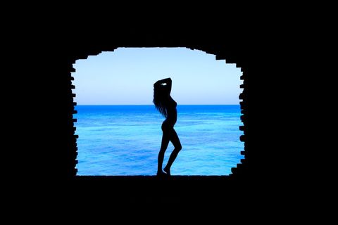 Silhouette of woman posing in brick frame overlooking ocean