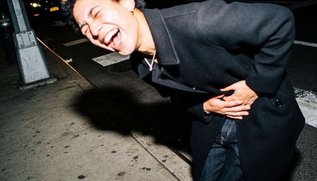 Young man laughing and clutching abdomen on urban sidewalk at night