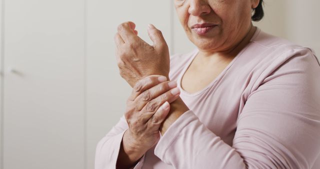 This stock photo shows a senior woman holding her wrist, likely experiencing pain. Ideal for use in health websites, articles about senior care, arthritis, injury recovery, healthcare advertisements, and educational materials. Visualizes themes of aging, healthcare, pain management, and physical discomfort.