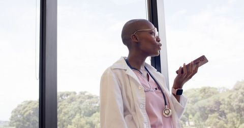 Female clinician holding smartphone and speaking at clinic window, stethoscope and smartwatch