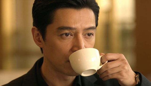 Contemplative asian man sipping coffee in warm cafe wearing dark blazer and wristwatch