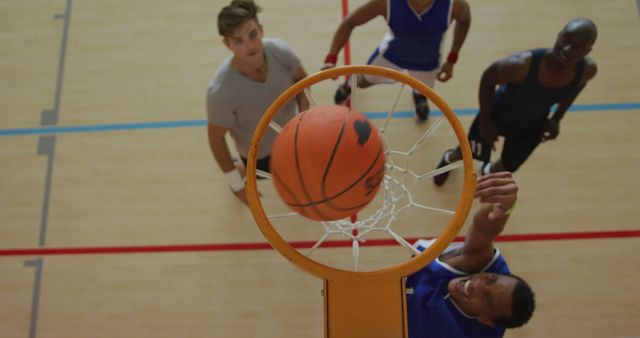 Basketball players are actively competing, trying to score by shooting the ball through the hoop. The image captures a dynamic moment from above, emphasizing action and competition, set in an indoor gym. Useful for illustrating sports articles, teamwork concepts, fitness campaigns, and promoting basketball events.