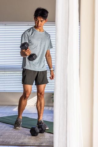 Asian man performing bicep curl with hex dumbbell on green mat during home workout