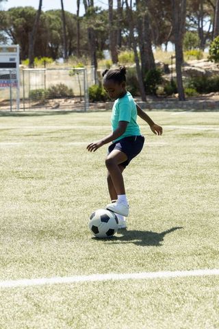 Young african american girl practicing soccer ball control on sunlit field