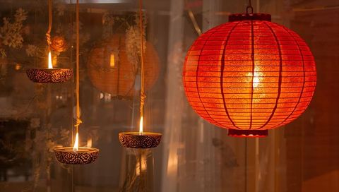 Red chinese lantern casting warm glow over hanging perforated candle bowls