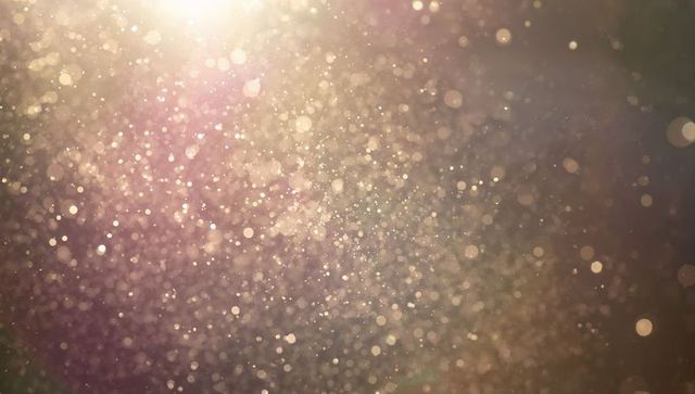 Golden bokeh particles floating in dreamy backlit dust field with shimmering lens flare