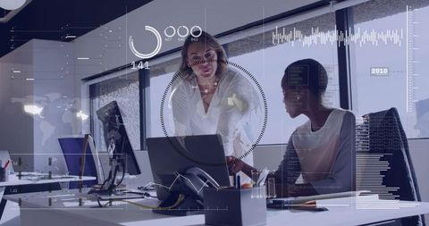 Coworkers collaborating over laptop with hud analytics overlays in open-plan office