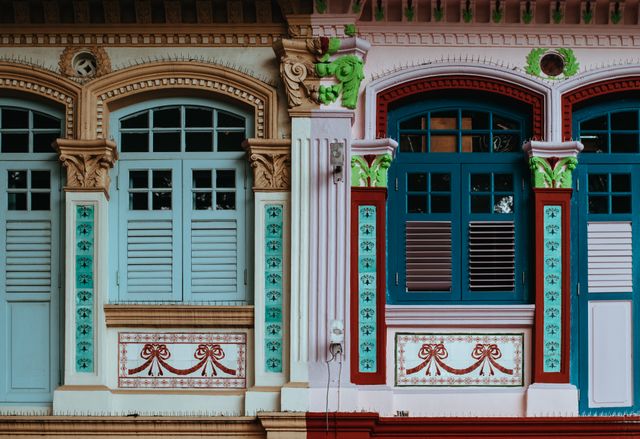 Vibrant traditional building facades featuring ornate windows with shutters. These buildings showcase intricate architectural designs and colorful decor, reflecting cultural heritage and historic significance. Ideal for use in travel blogs, architectural studies, heritage preservation projects, and tourism promotions.