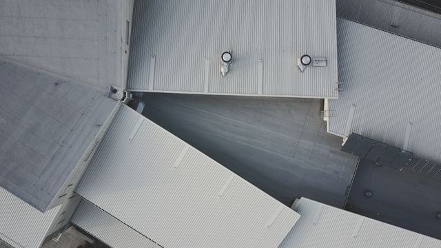 An aerial perspective of industrial building rooftops showcasing geometric patterns and minimalistic design in grey tones. Suitable for architectural design presentations, urban planning projects, industrial and manufacturing marketing materials, or background imagery for technical documents.