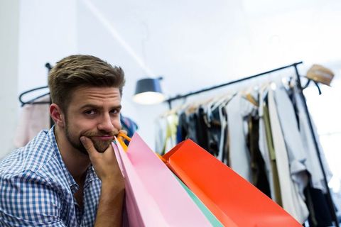 Man Shopping Reluctantly Leaning on Colorful Bags in Clothing Store