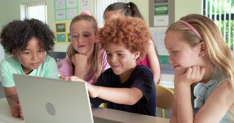 Multicultural children collaborating around laptop in classroom learning technology